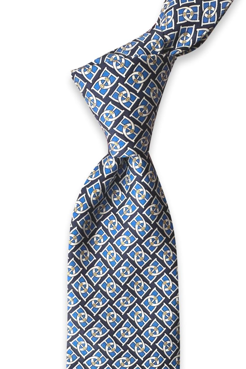 Knotted navy silk twill tie showing blue geometric motifs and ivory chain links with gold accents