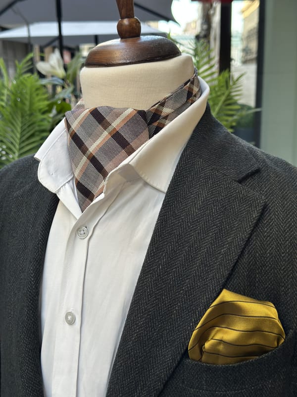 Brown and taupe plaid silk ascot displayed with a white shirt and charcoal jacket